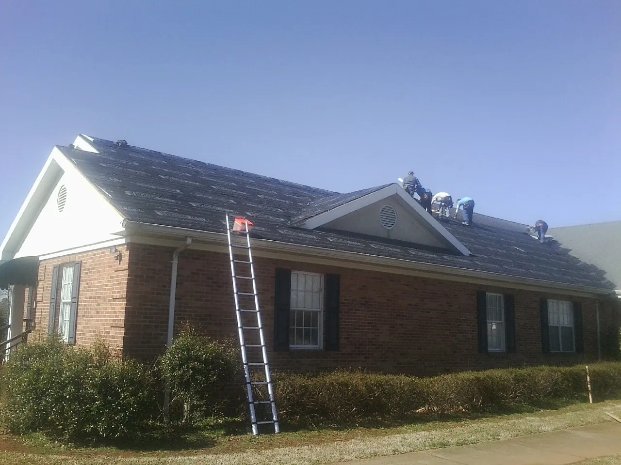 Crew tearing shingles off a brick ranch roof with a ladder set in Topsfield