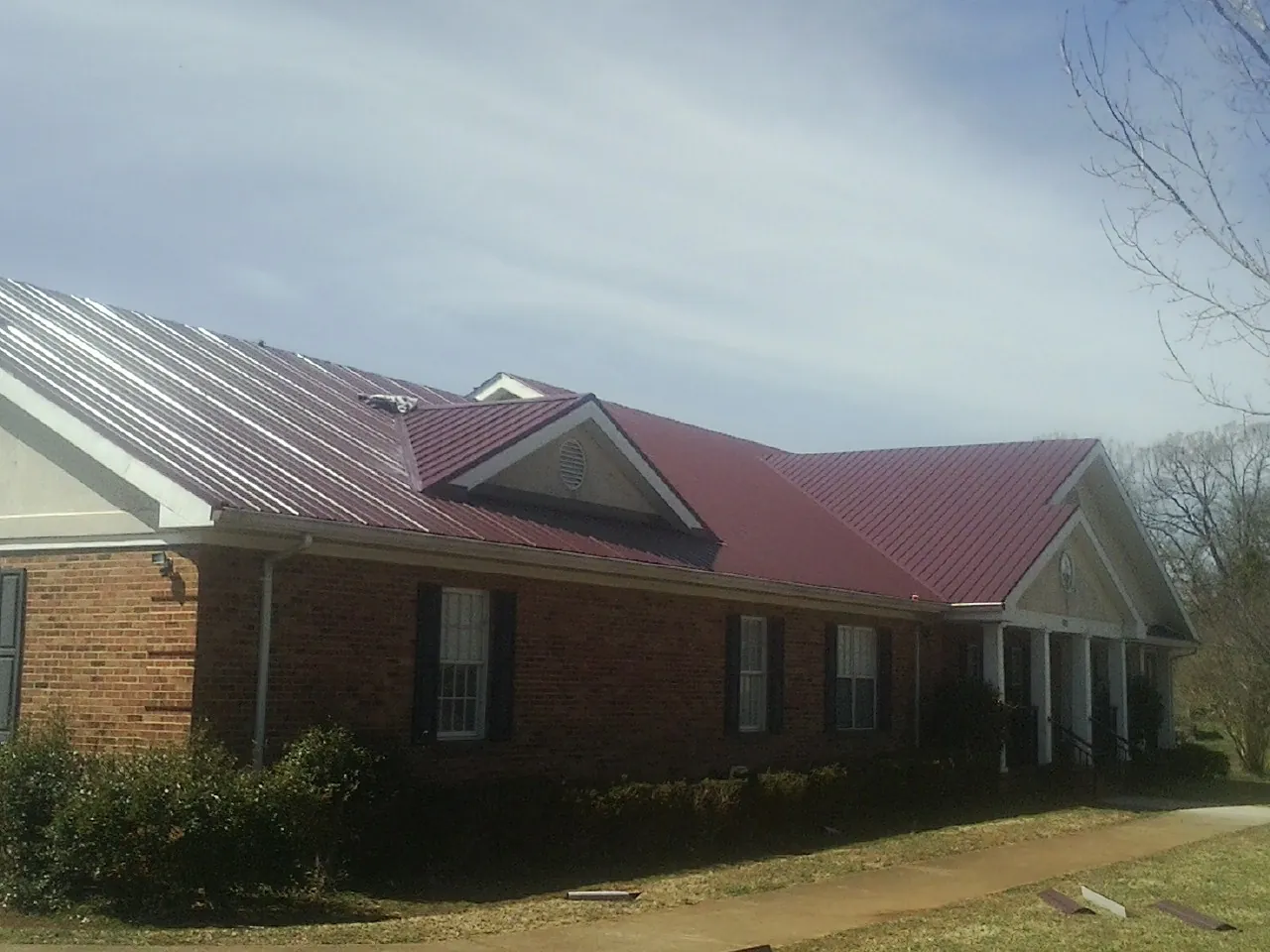 Red metal roof with gabled entries on a long brick building, from a Hail Damage Roof Repair job in Topsfield