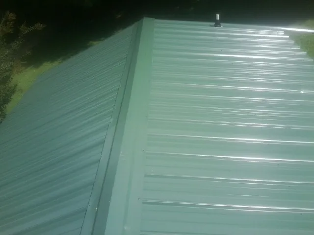 New green metal panels meeting at the ridge of a roof — Flat Roof Repair work by our crew in Topsfield