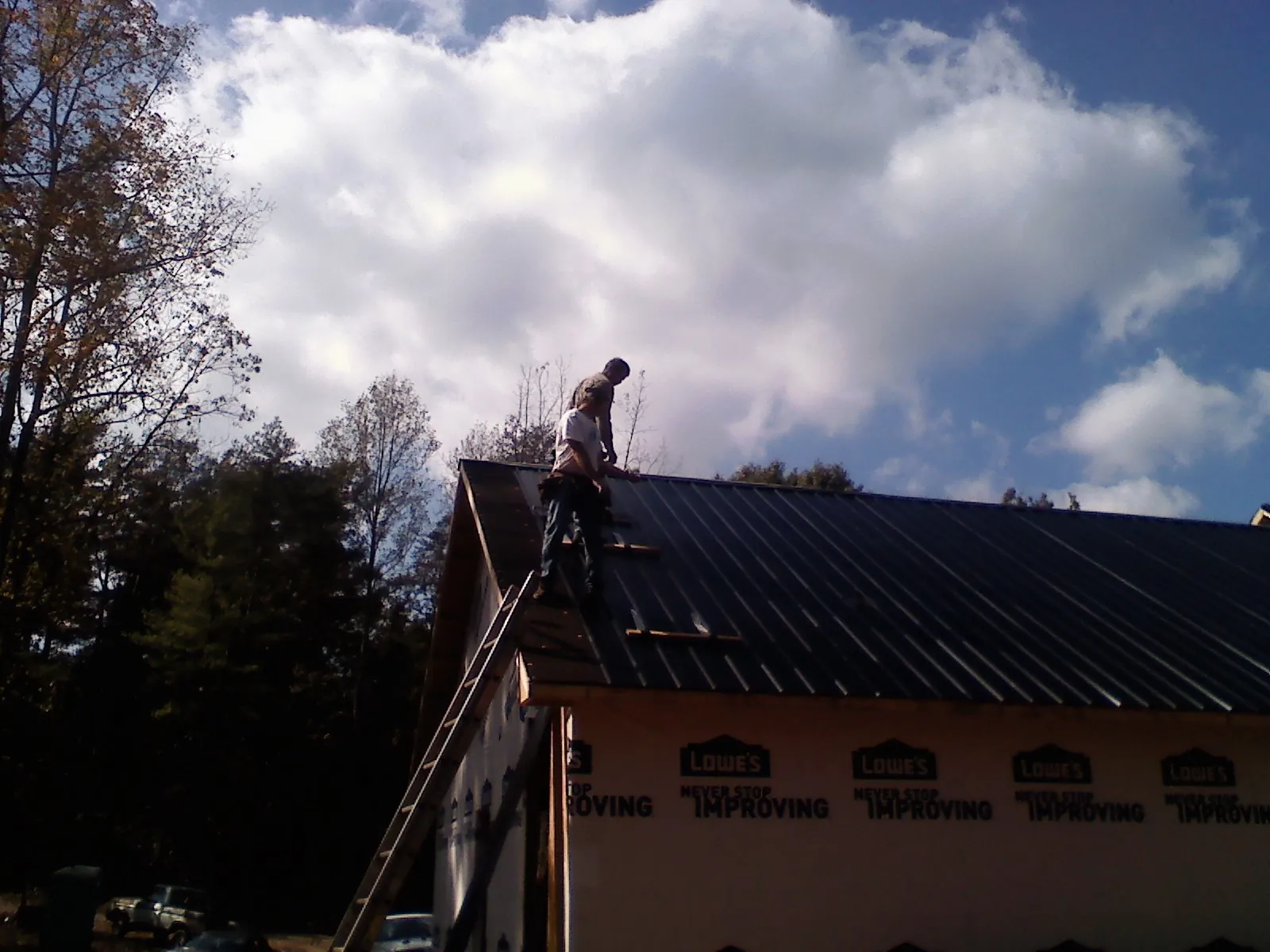Roofer fastening dark metal panels high against a cloudy sky, from a Roof Inspection job in Topsfield