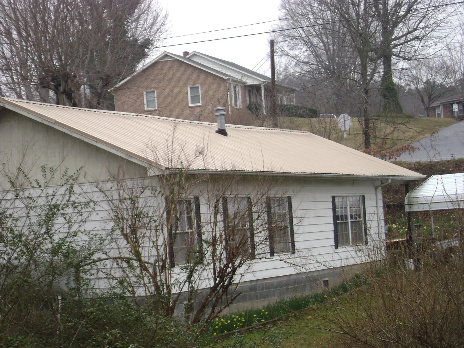Tan metal roof on a white sided house set into a hillside — Commercial Roofing by Roofing Brothers in Topsfield